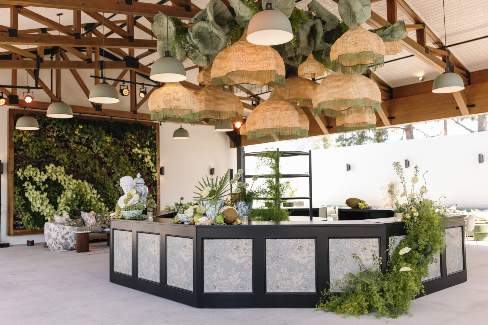 Bar at The Colony House beneath rattan pendant lights, with a living wall behind.
