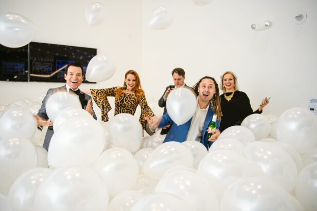 four industry professionals at a holiday party cheering in a room of white balloons