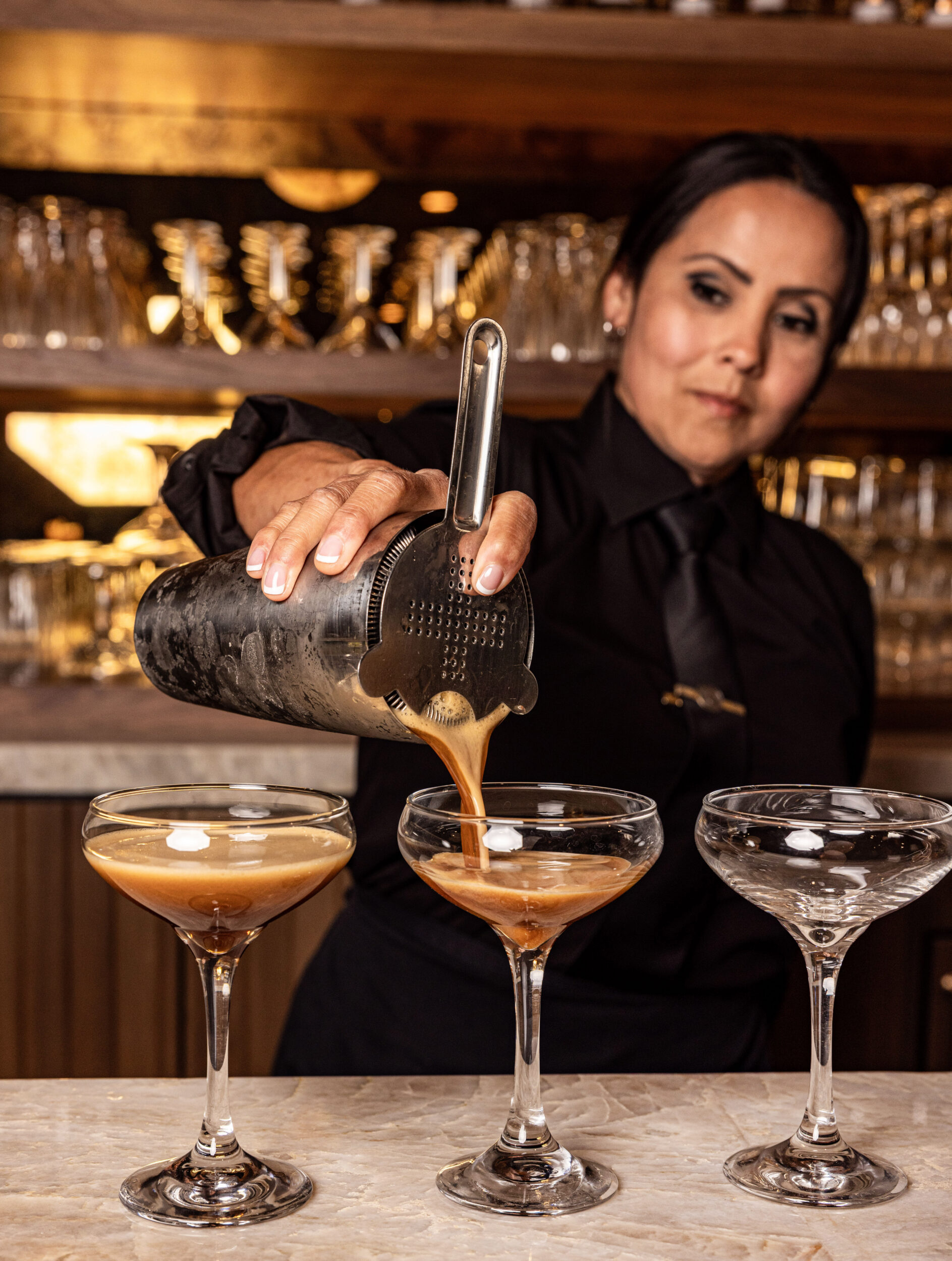 Bartender pouring espresso martinis into coupe glasses.