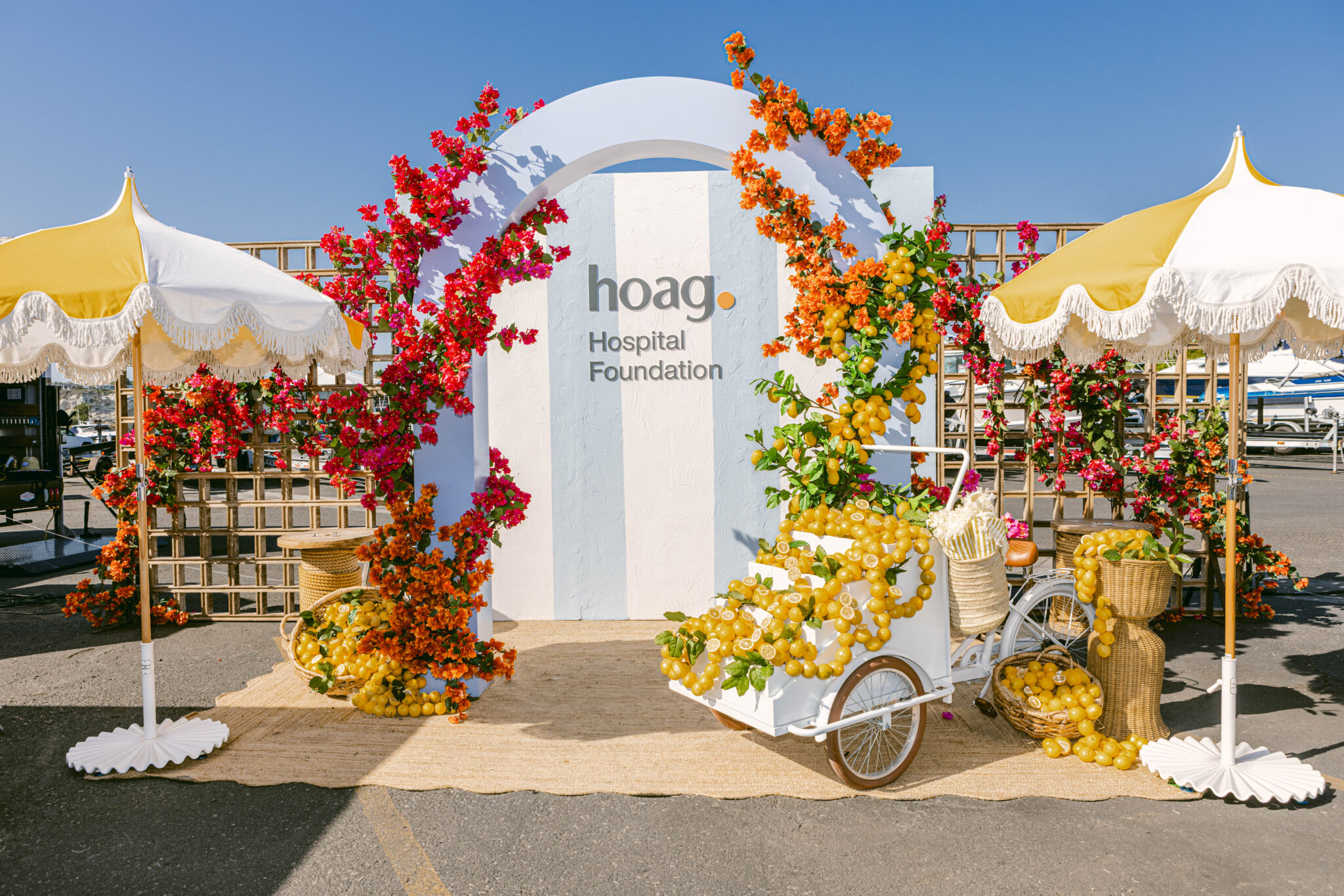 Hoag Hospital Foundation arch display with a lemon cart, red flowers and yellow scalloped umbrellas.